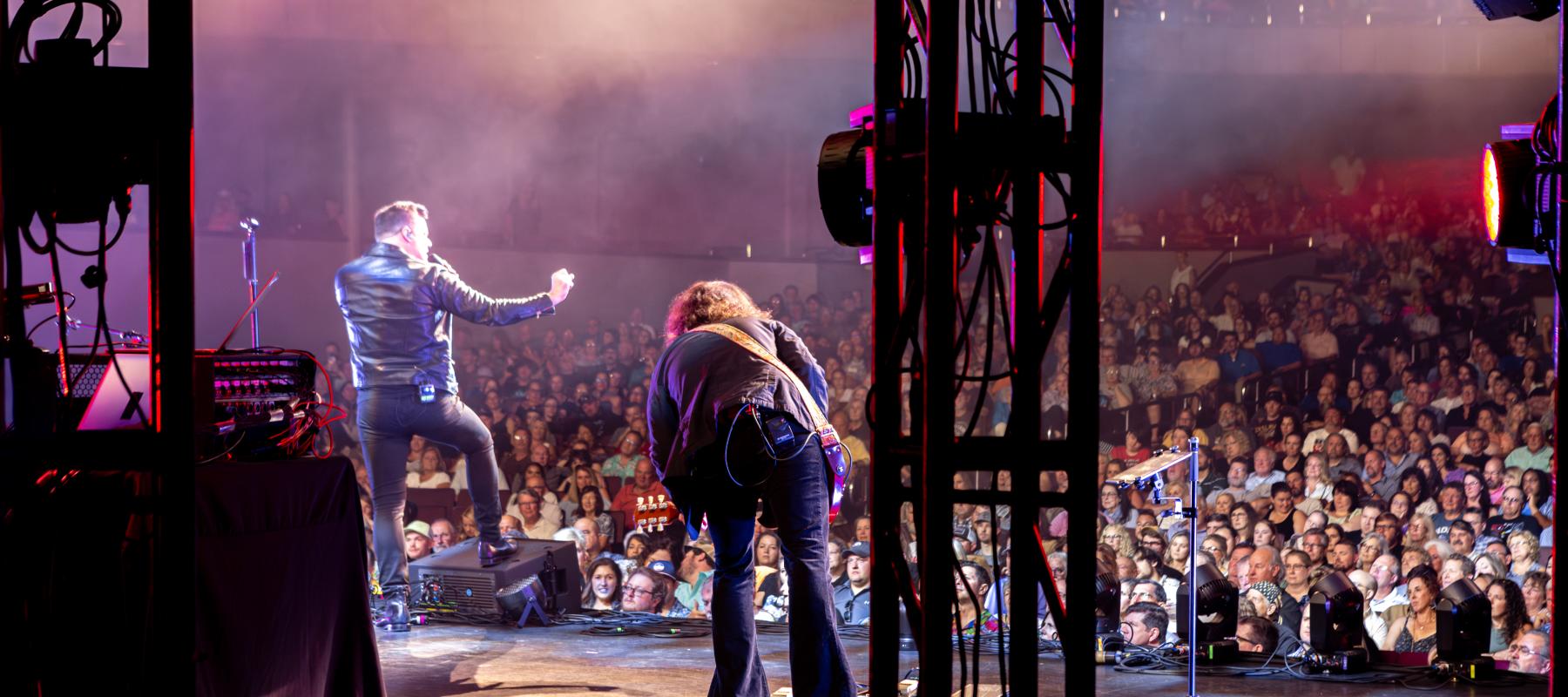 A shot of a singer performing to a crowd. The gutarist is also pictured performing.