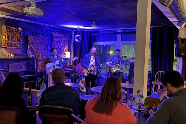 people sit in tables and listen to band performing at the Woodshop Listening Room