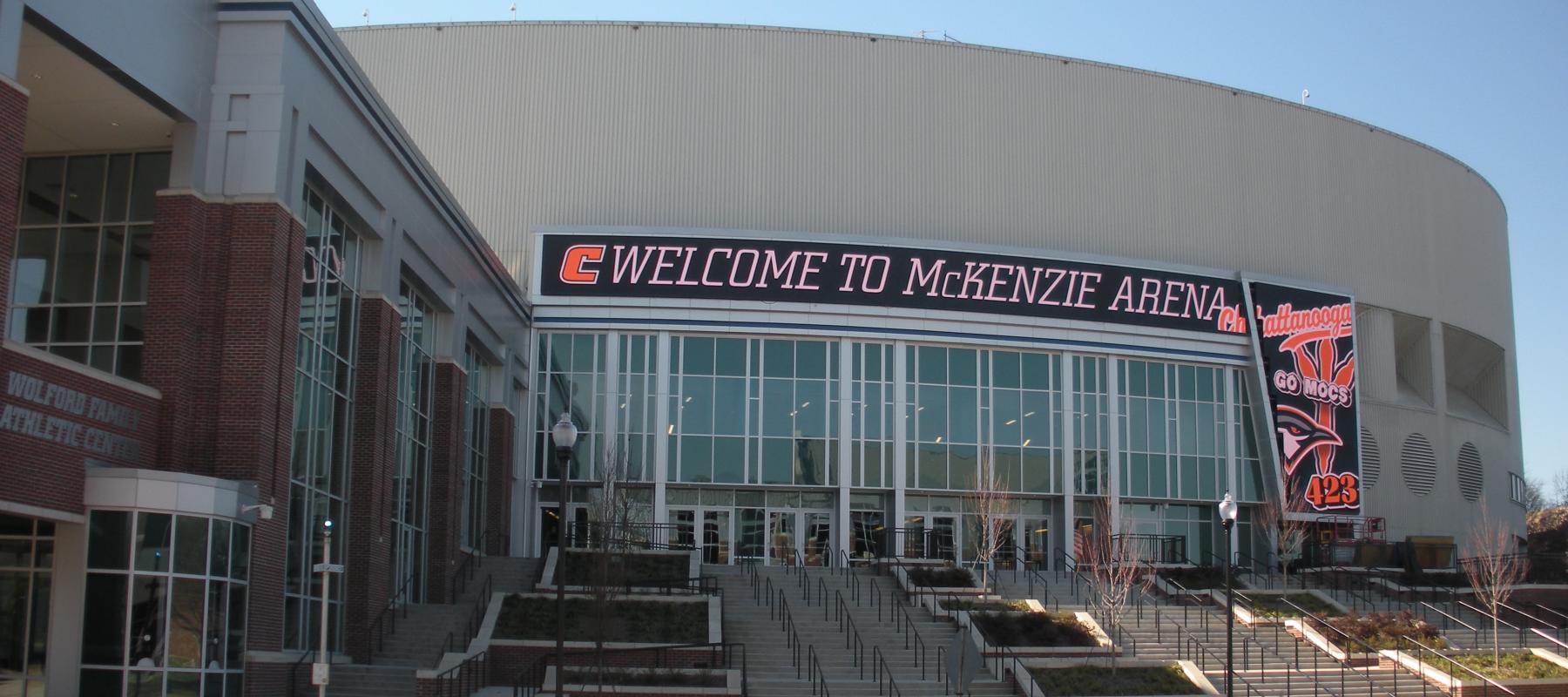 Outside of Sports arena. Large sign saying "Welcome to McKenzie Arena". Stairs leading up to big windows.