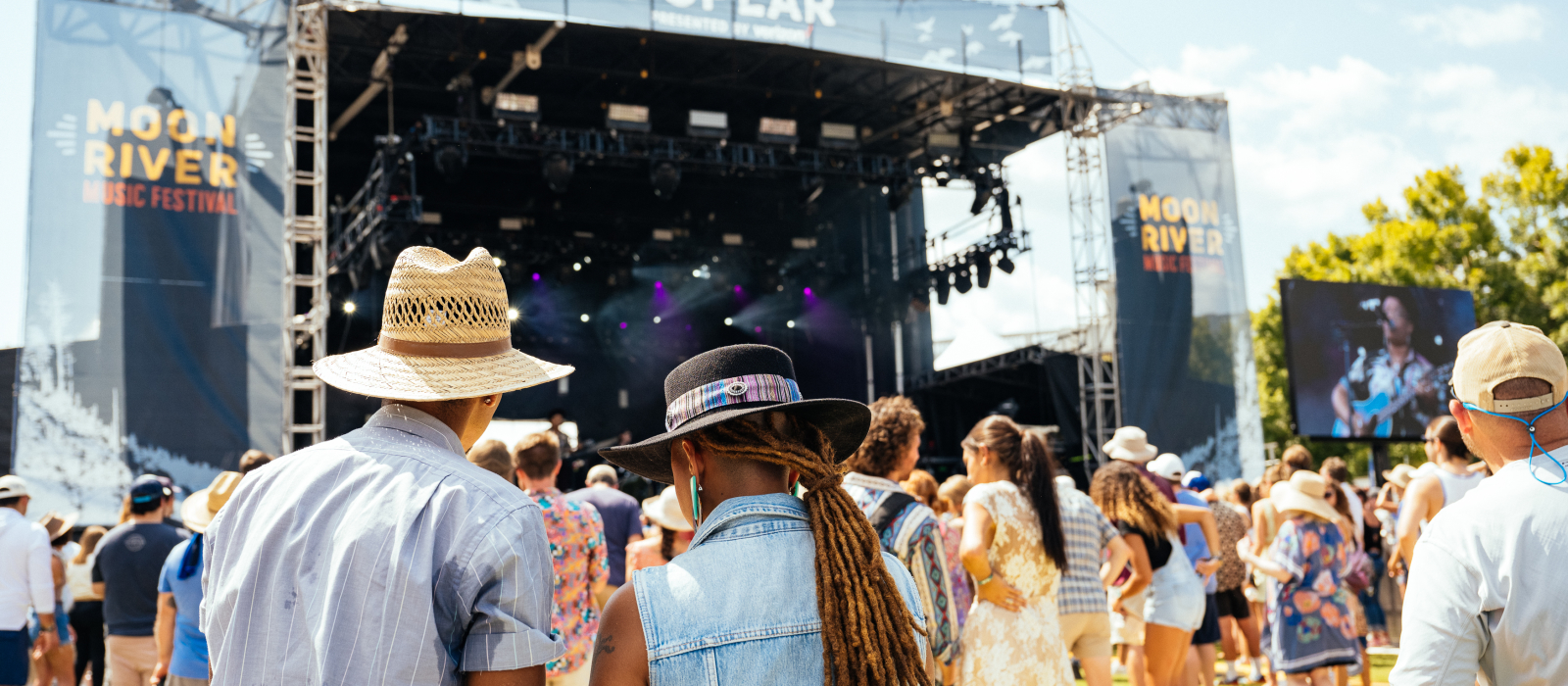 Photo taken from behind as man and woman walk towards stage of Moon River Festival
